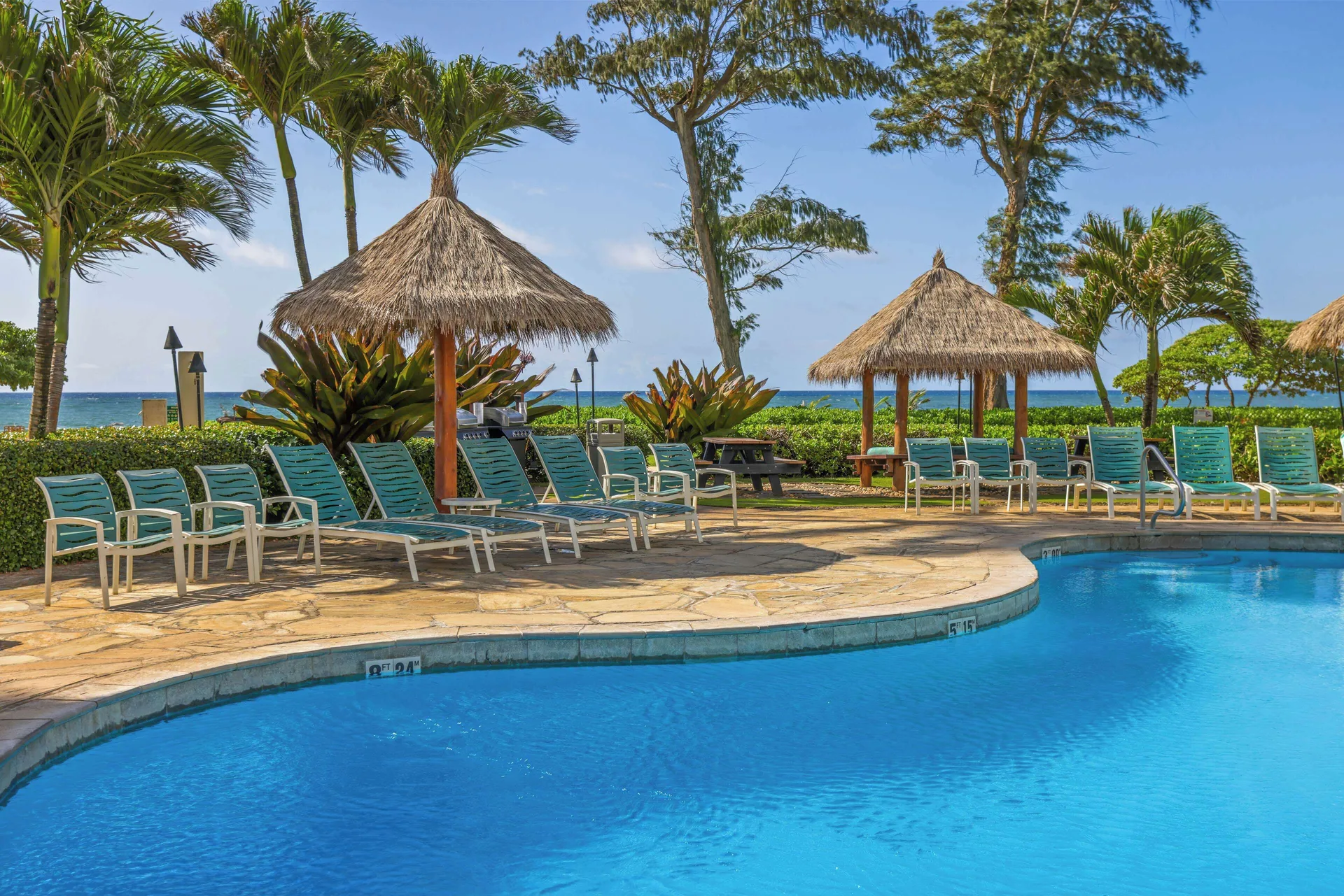 Pool deck with lounge chairs and thatched shade huts at Aston Islander on the Beach.