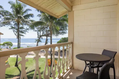 Ocean View room balcony with table, chairs, palms, lawn, and ocean at Aston Islander on the Beach.