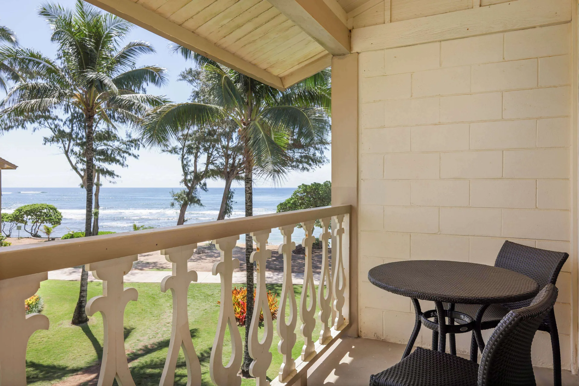 Ocean View room balcony with table, chairs, palms, lawn, and ocean at Aston Islander on the Beach.
