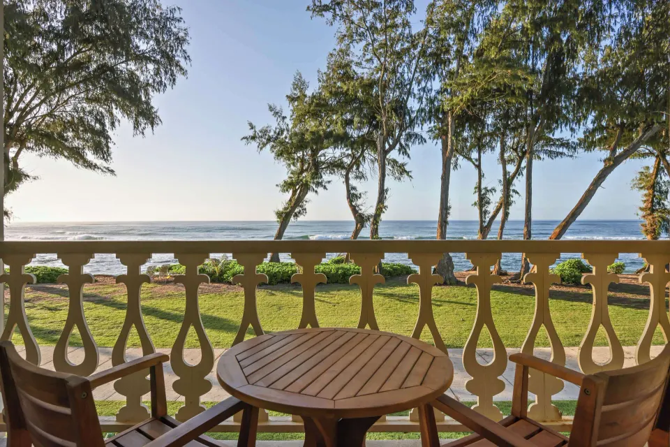 Oceanfront balcony with table, chairs, lawn, trees, and ocean view at Aston Islander on the Beach.
