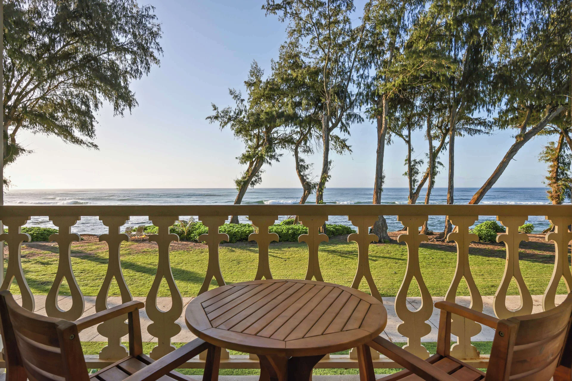 Oceanfront balcony with table, chairs, lawn, trees, and ocean view at Aston Islander on the Beach.