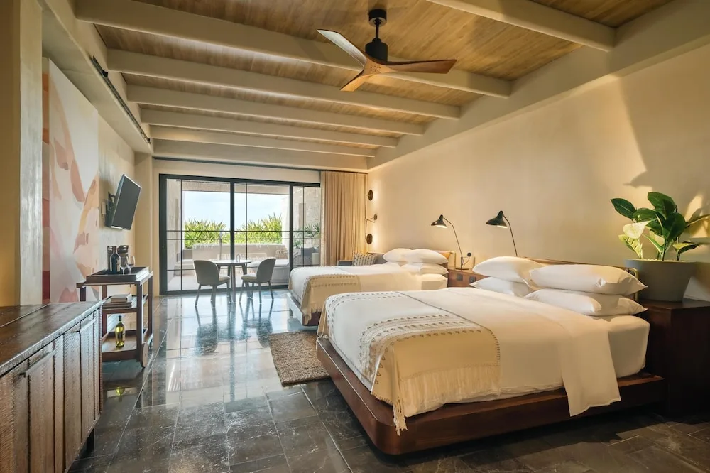 Two-bed guest room with terrace doors and warm wood ceiling at Atelier Playa Mujeres.