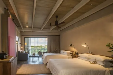 Junior Suite with two beds, balcony doors, sitting area, and wood ceiling at Atelier Playa Mujeres.