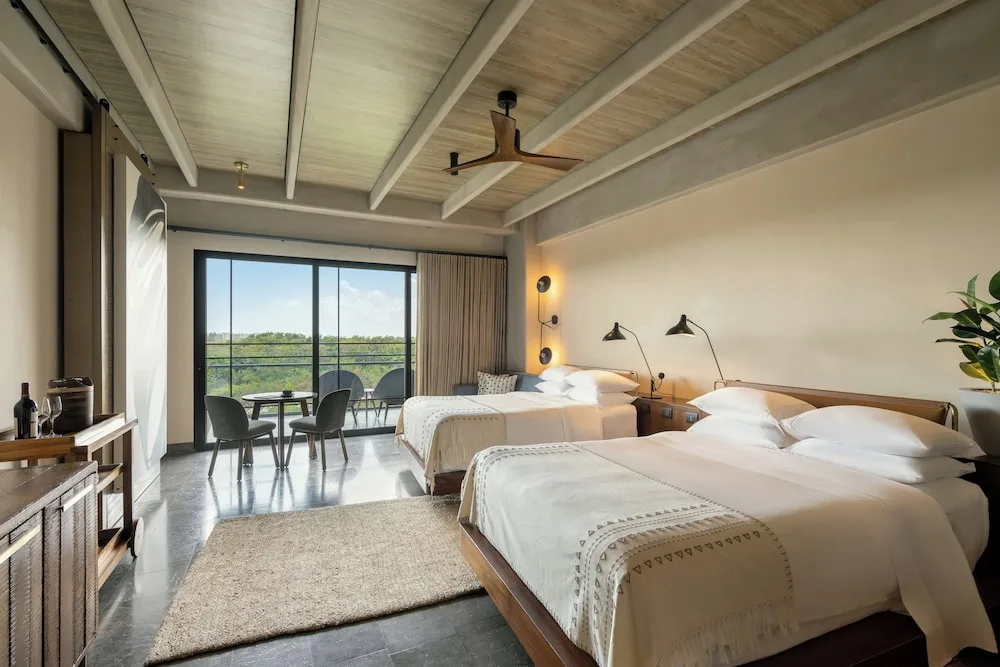 Junior Suite with two beds, balcony seating, and minibar cabinet at Atelier Playa Mujeres.