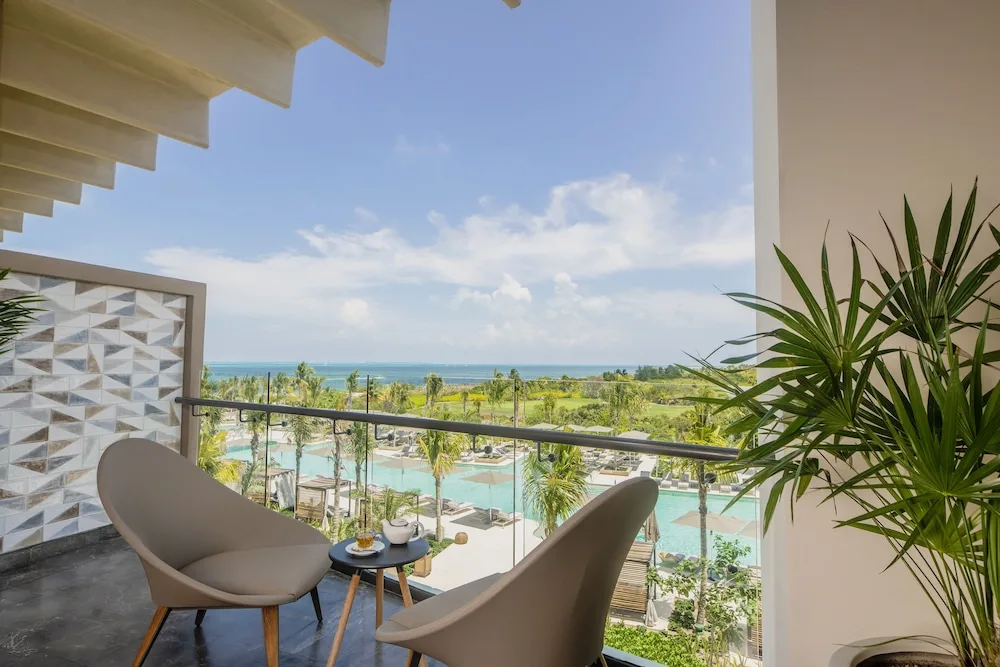 Balcony seating with pool, palms, and ocean view at Atelier Playa Mujeres.