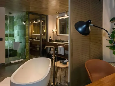 Junior Suite bath area with soaking tub, vanity, shower, chair, and floor lamp at Atelier Playa Mujeres.