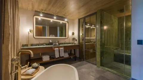 Junior Suite bathroom with tub in foreground and glass shower at Atelier Playa Mujeres.
