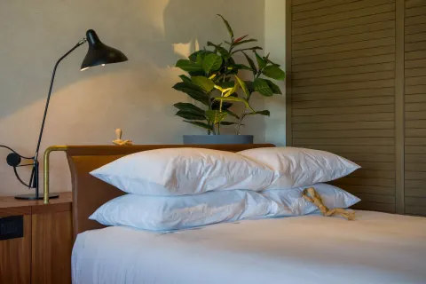 Junior Suite king bed pillows with bedside lamp and plant at Atelier Playa Mujeres.