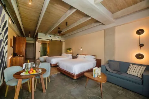 Junior Suite with two beds, sofa, table, and bath beyond at Atelier Playa Mujeres.