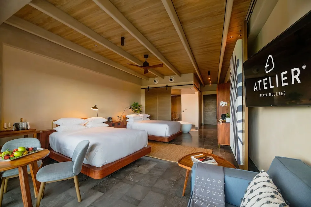 Two beds, sofa seating, and TV in a Wheelchair Accessible Junior Suite at Atelier Playa Mujeres.
