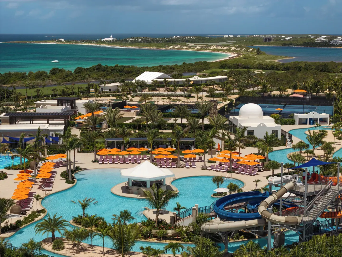 Aerial view of pools, slides, orange umbrellas, and coastline at Aurora Anguilla Resort & Golf Club.