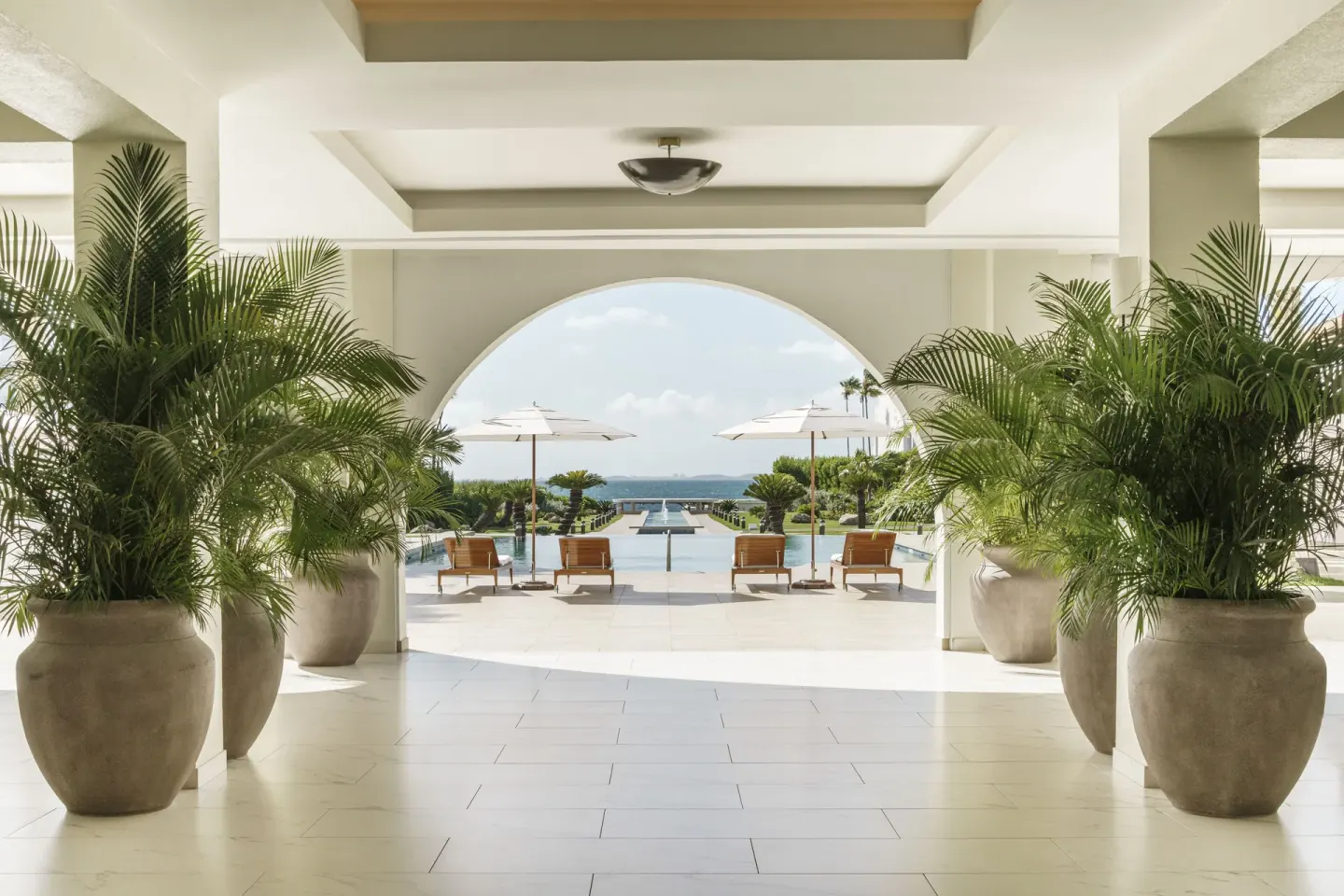 Arched lobby walkway with potted palms and pool view at Aurora Anguilla Resort & Golf Club.