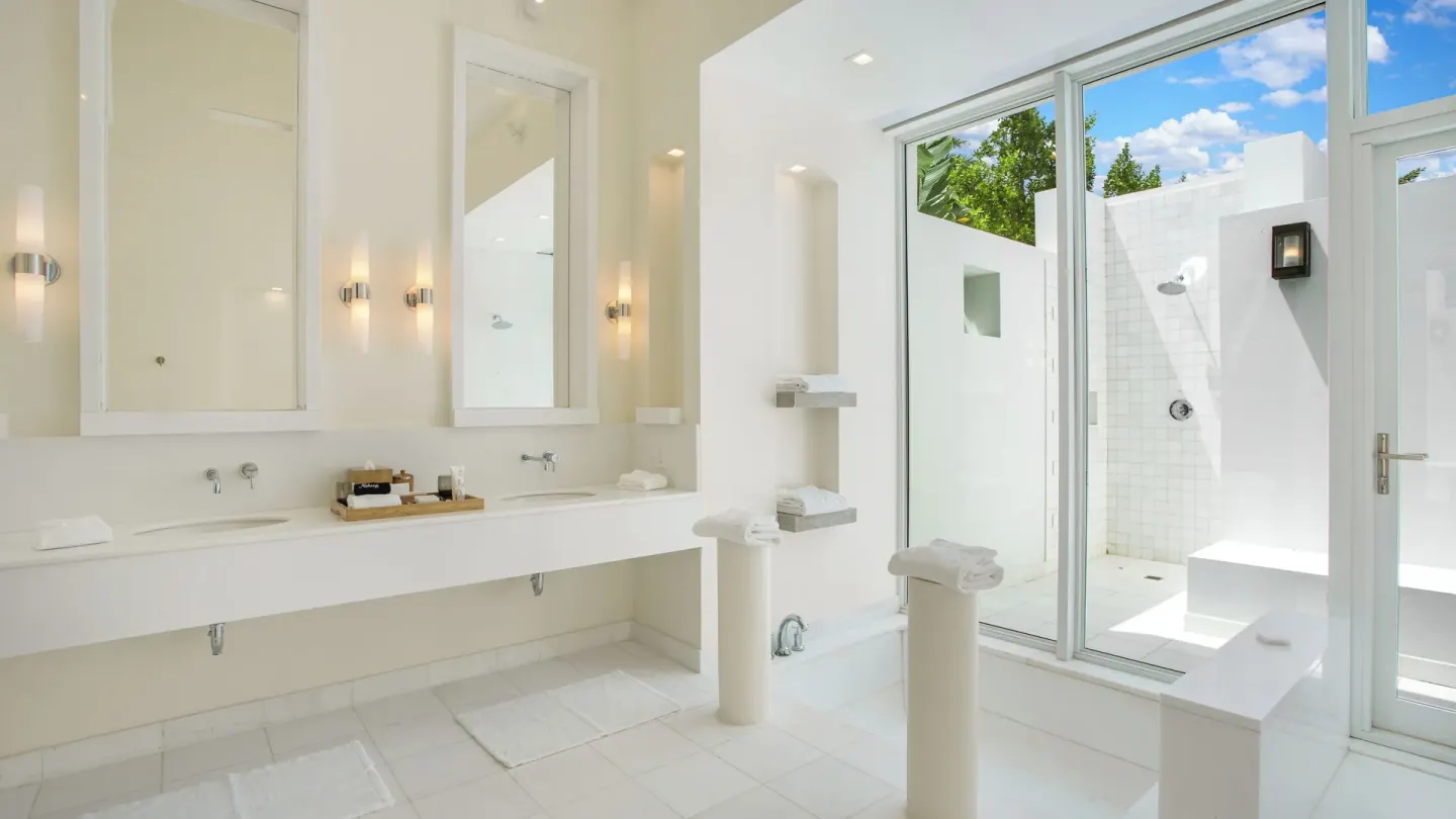 White bathroom with dual vanities and an outdoor shower at Aurora Anguilla Resort & Golf Club.