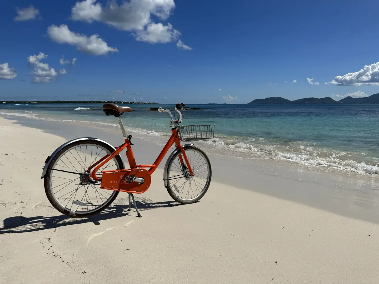 Orange bicycle on the beach at Aurora Anguilla Resort & Golf Club with turquoise water beyond.