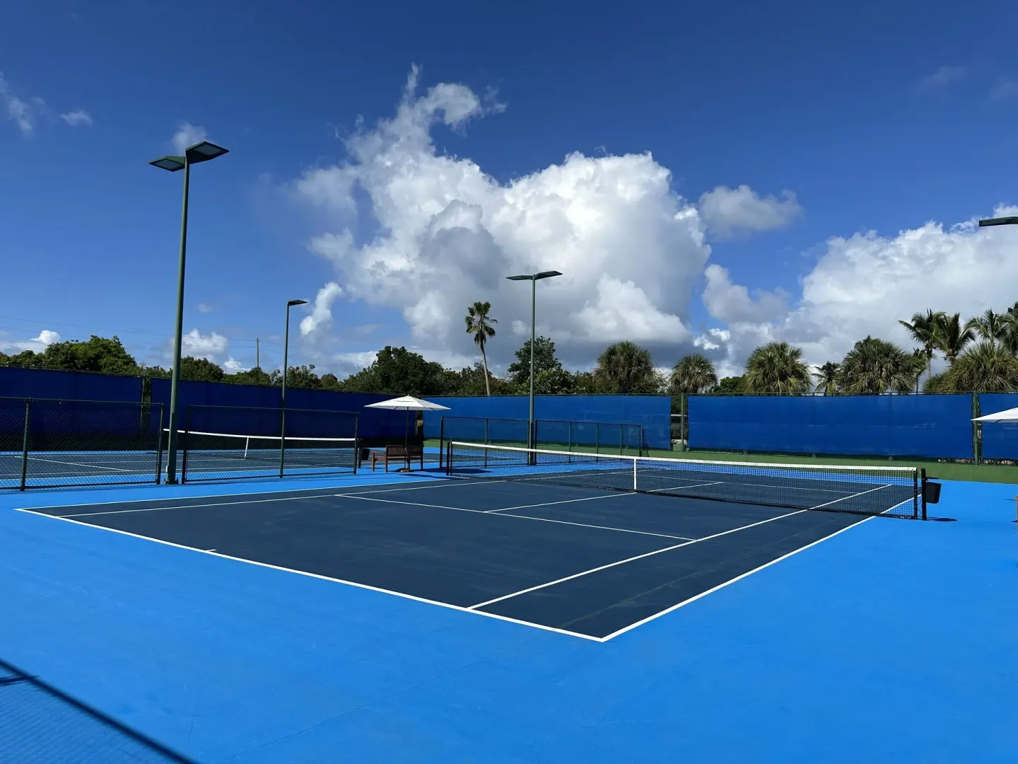 Blue tennis courts at Aurora Anguilla Resort & Golf Club under a bright cloud-filled sky.