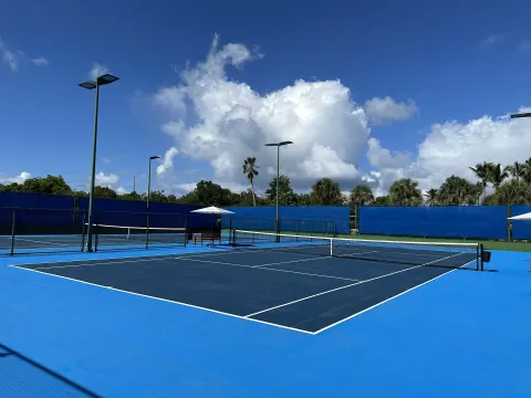 Blue tennis courts at Aurora Anguilla Resort & Golf Club under a bright cloud-filled sky.