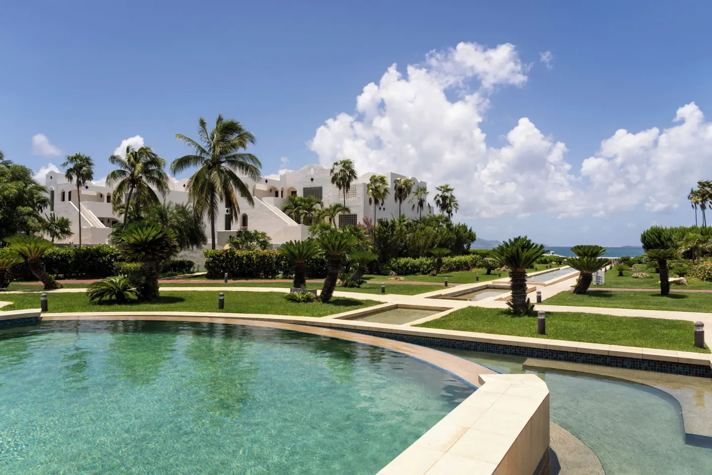 Curved resort pool, palms, lawns, and white buildings at Aurora Anguilla Resort & Golf Club.