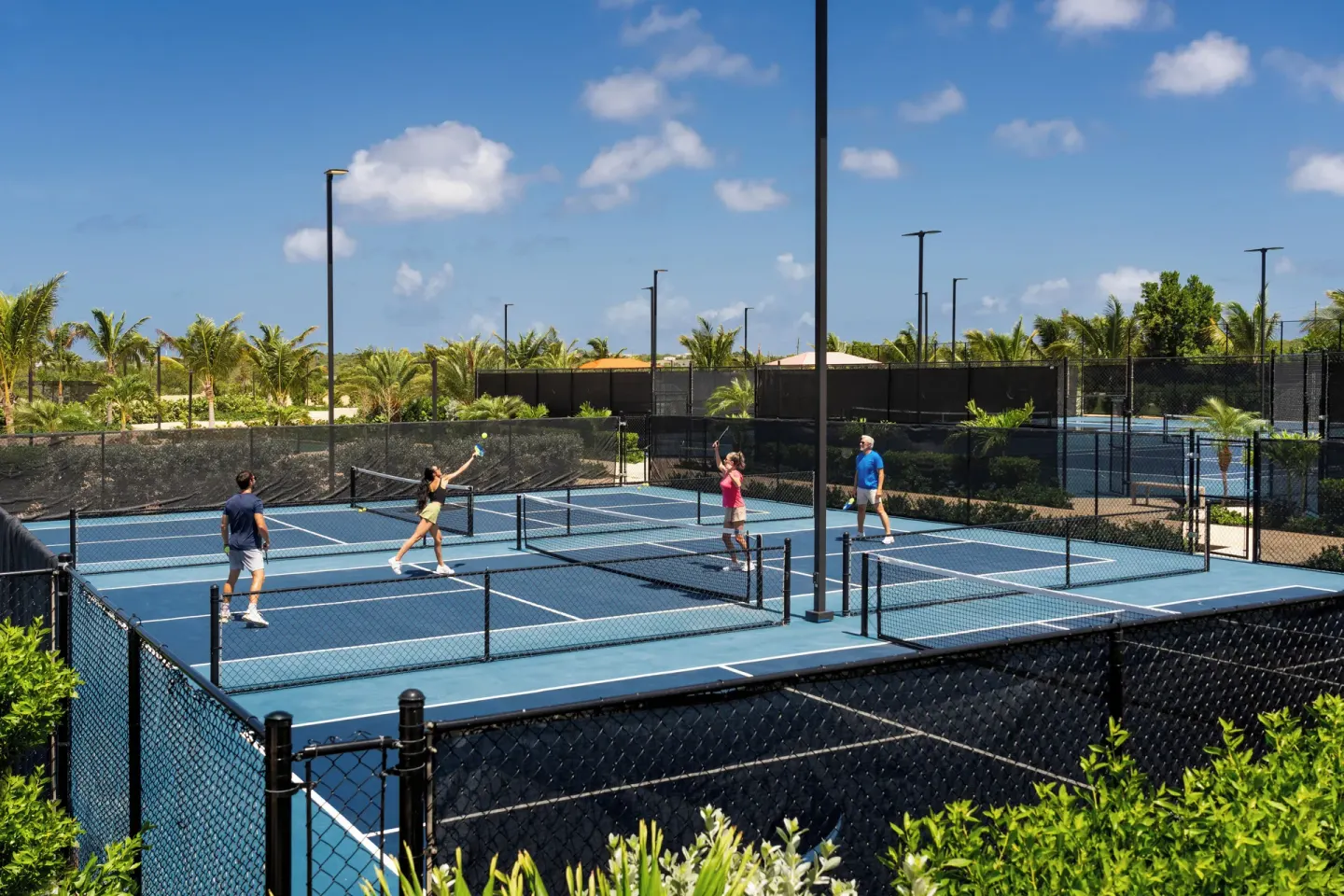 Guests play on blue pickleball courts at Aurora Anguilla Resort & Golf Club surrounded by palms.
