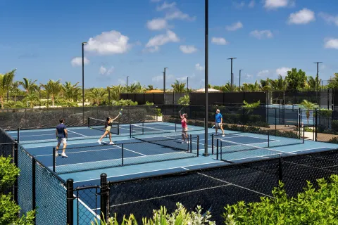 Guests play on blue pickleball courts at Aurora Anguilla Resort & Golf Club surrounded by palms.
