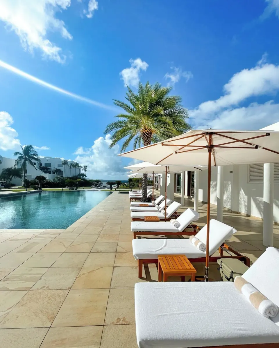 White loungers and umbrellas line a sunny pool deck at Aurora Anguilla Resort & Golf Club.