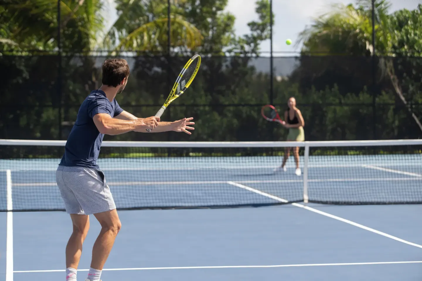 Two guests play tennis on a blue court at Aurora Anguilla Resort & Golf Club.