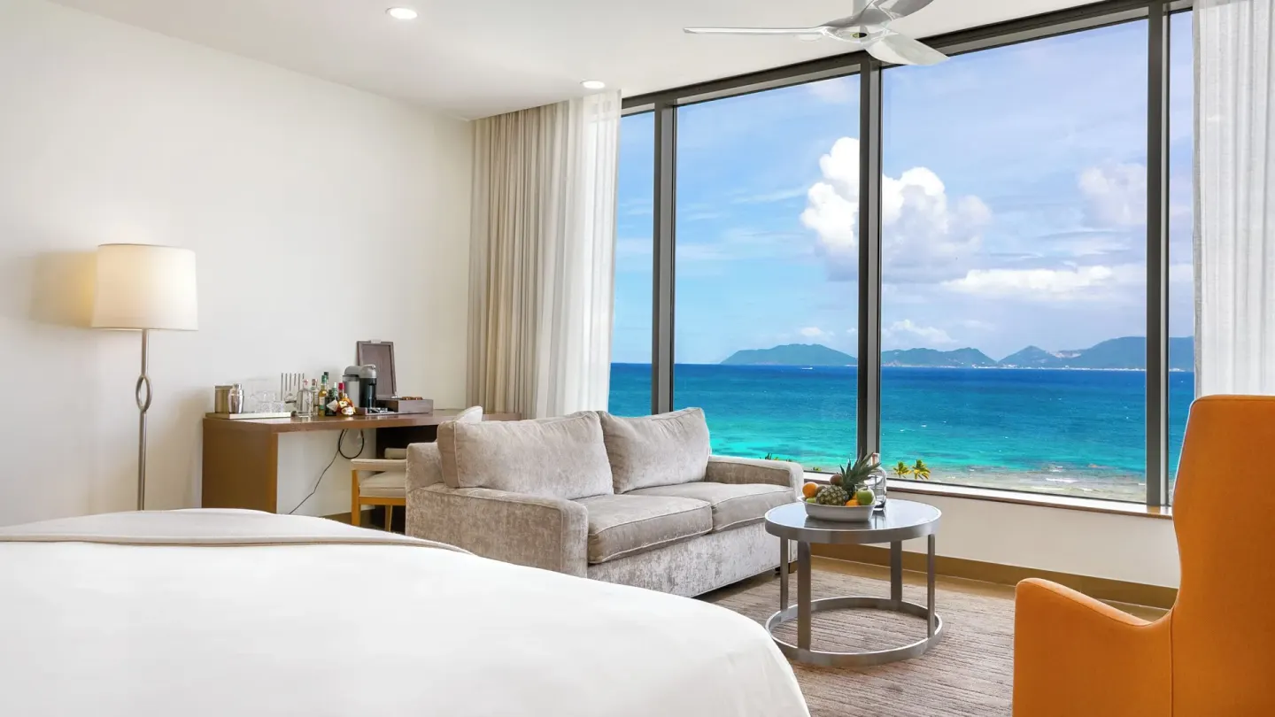 Ocean View Deluxe Room sofa and king bed beside ocean windows at Aurora Anguilla Resort & Golf Club.