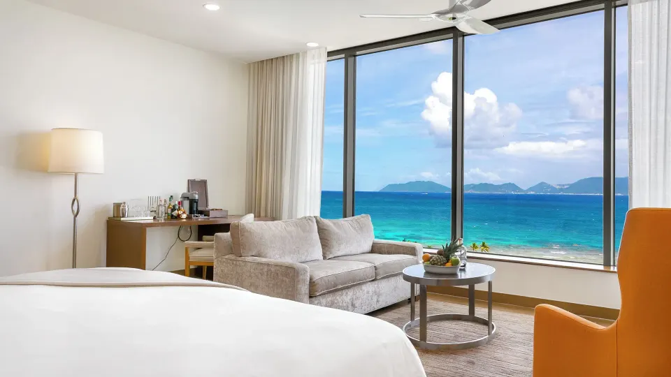 Ocean View Deluxe Room sofa and king bed beside ocean windows at Aurora Anguilla Resort & Golf Club.