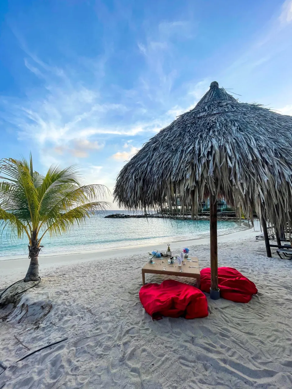 Beach lounge setup with red cushions under a thatched umbrella at Avila Beach Hotel.
