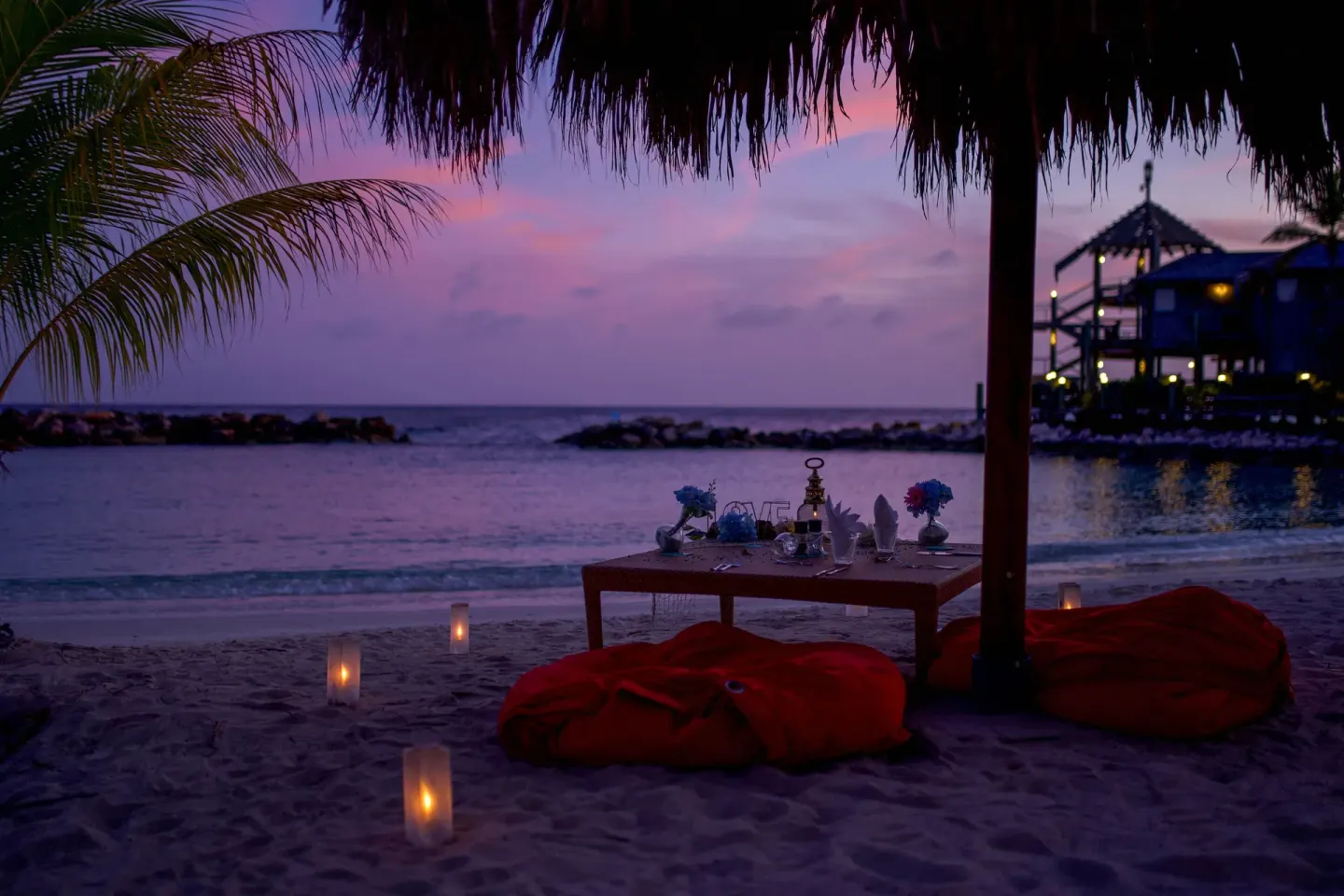 Candlelit beach lounge setup at dusk with ocean and pavilion views at Avila Beach Hotel.