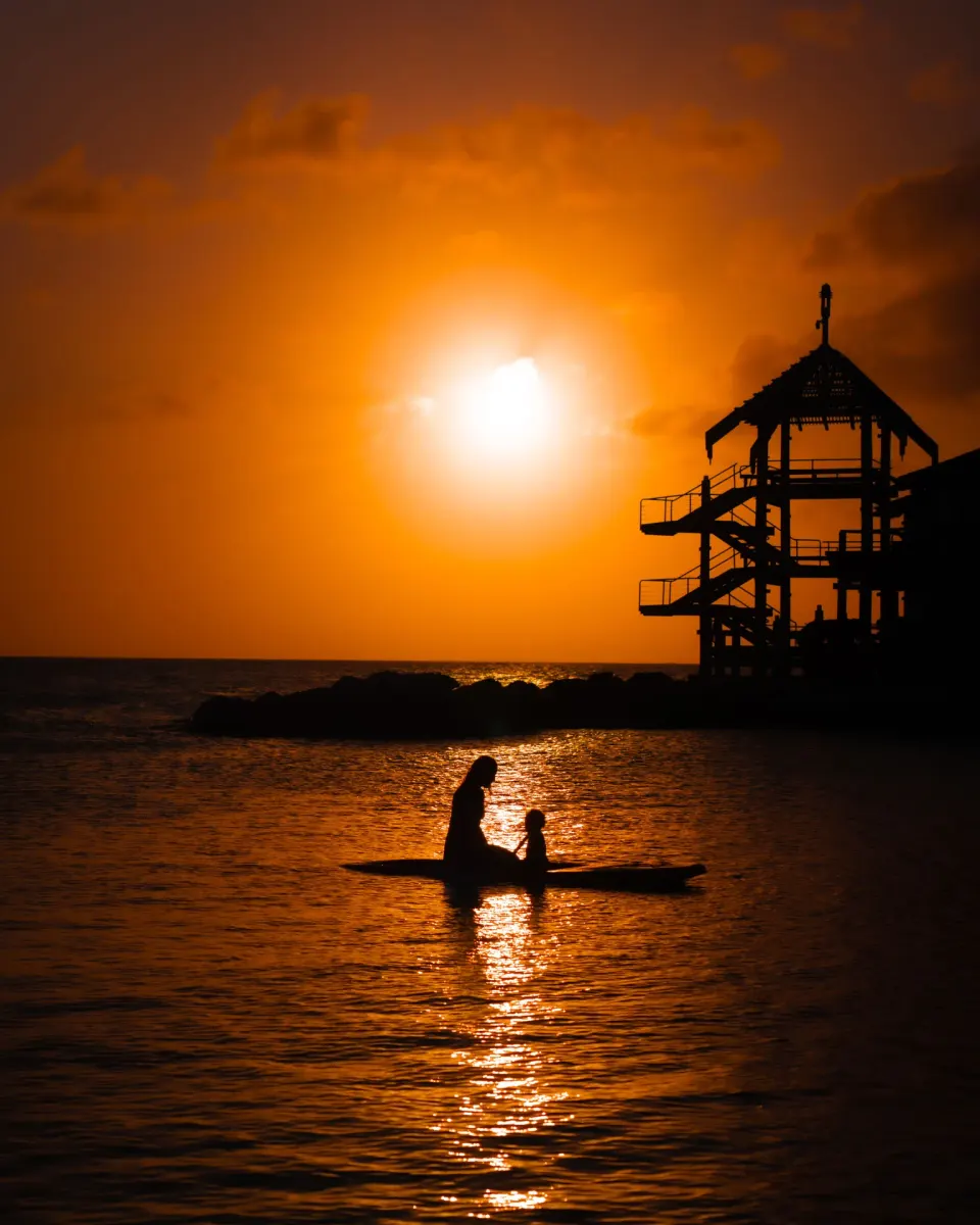A paddleboard silhouette crosses the water at sunset near Avila Beach Hotel.