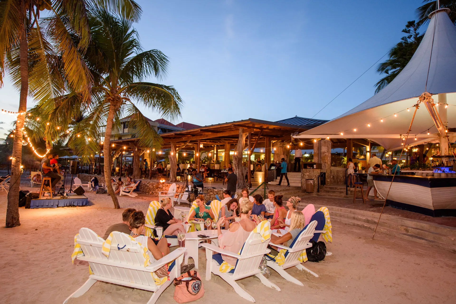 Evening beach bar scene with guests, palm trees, and string lights at Avila Beach Hotel.