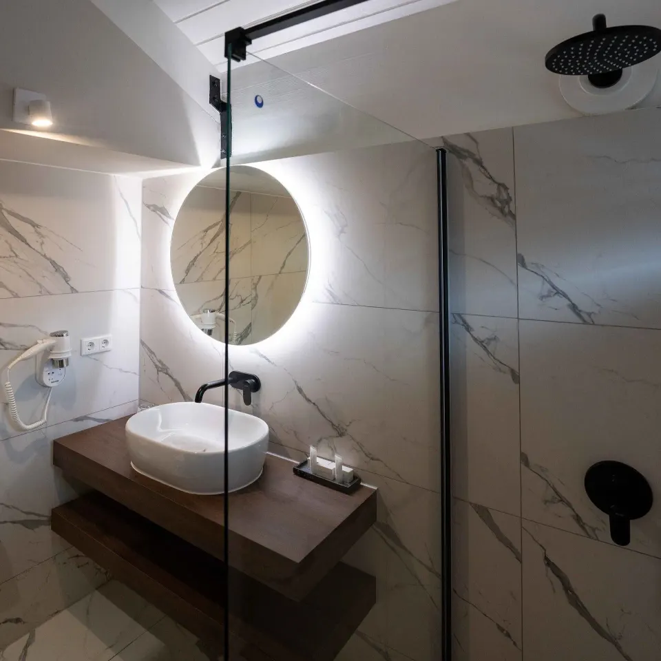 Bathroom with round lit mirror and rainfall shower in a Deluxe Oceanfront Room at Avila Beach Hotel.