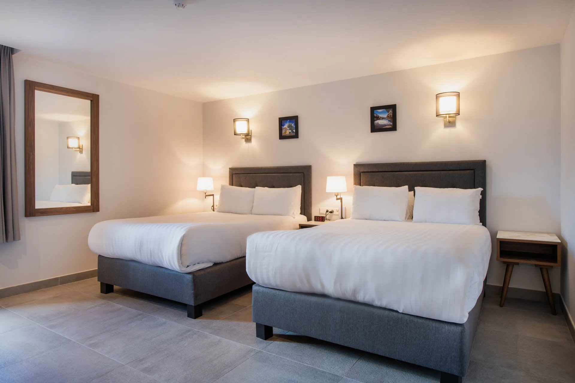 Bedroom with two double beds and wall mirror at Avila Beach Hotel.