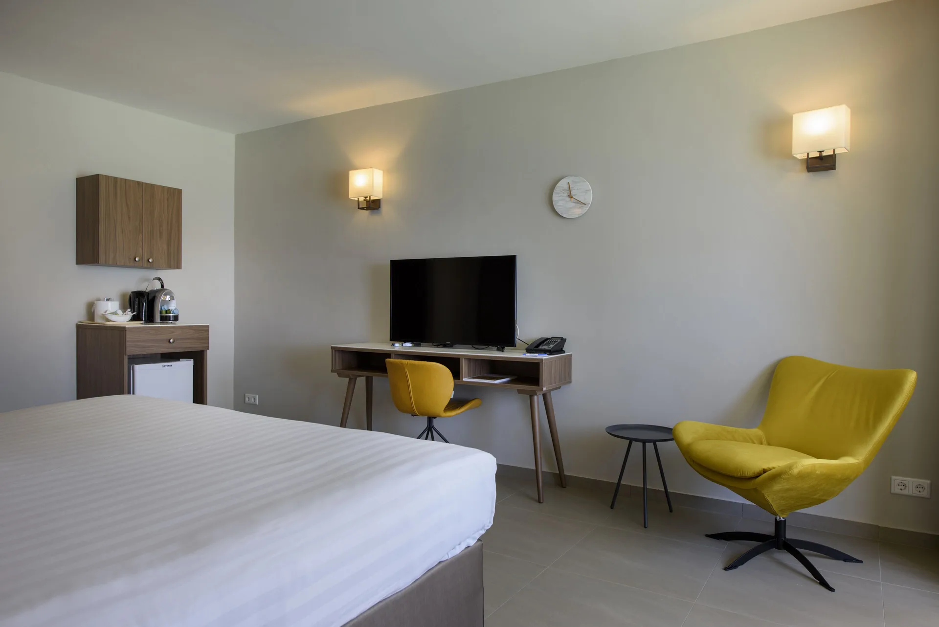 Standard Room with bed, TV desk, mini fridge and yellow lounge chair at Avila Beach Hotel.