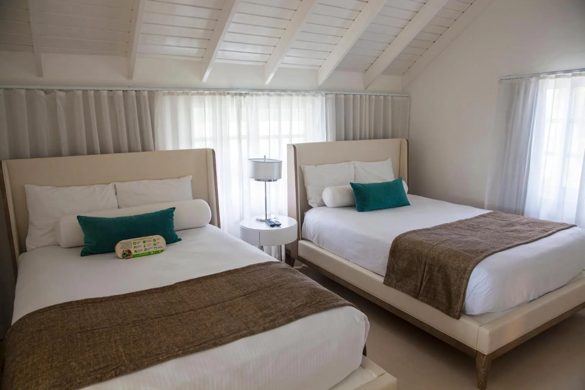 Guest room at Azul Beach Resort Negril with two beds, teal pillows and a white beamed ceiling.