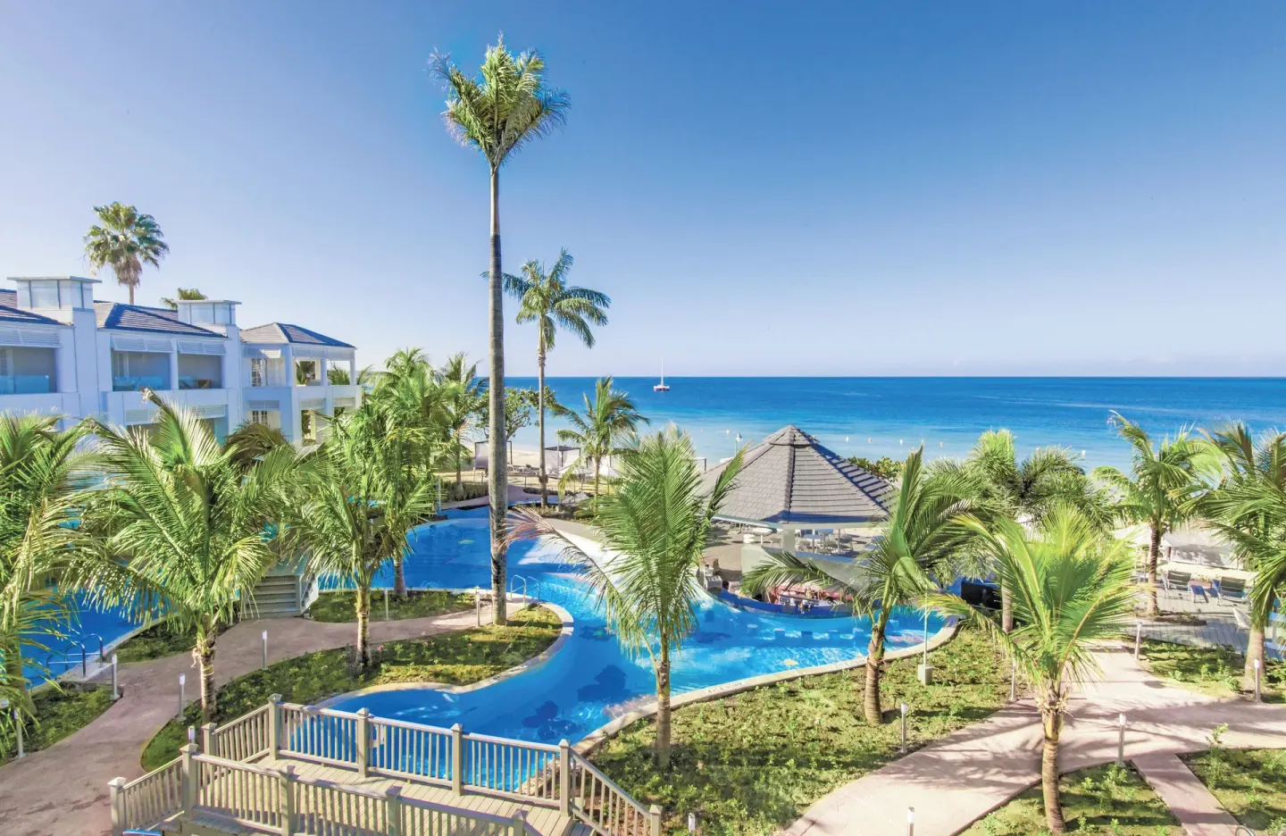 Pool, palms, resort buildings, and ocean beyond the beach at Azul Beach Resort Negril.