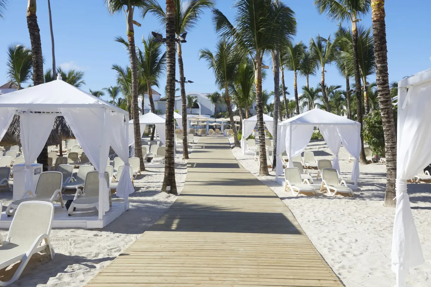 Palm-lined beach walkway with white cabanas at Bahia Principe Escape Ambar.