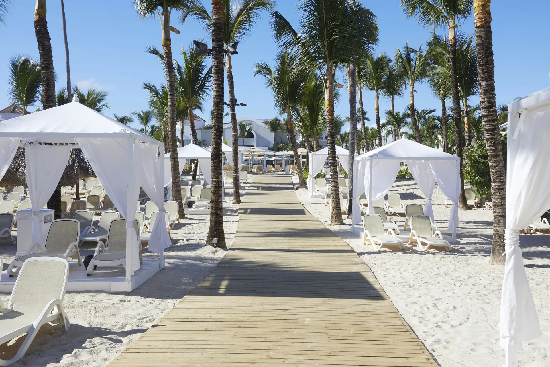 Palm-lined beach walkway with white cabanas at Bahia Principe Escape Ambar.
