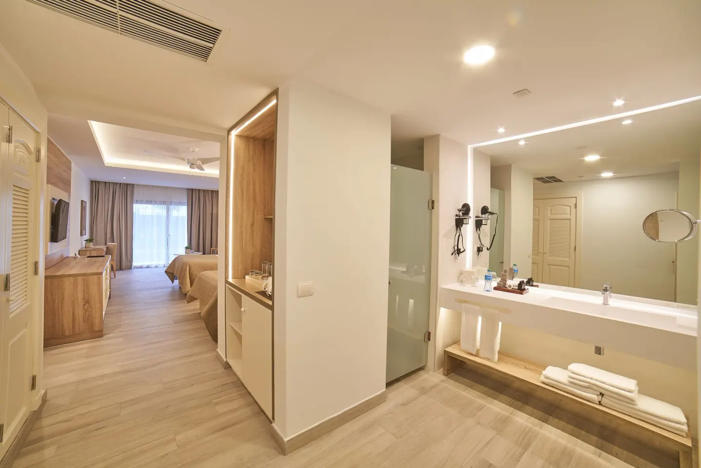 Guest room bathroom vanity and bedroom with two beds at Bahia Principe Escape Ambar.