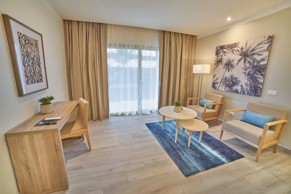 Junior Suite Deluxe lounge with desk and balcony curtains at Bahia Principe Escape Ambar.