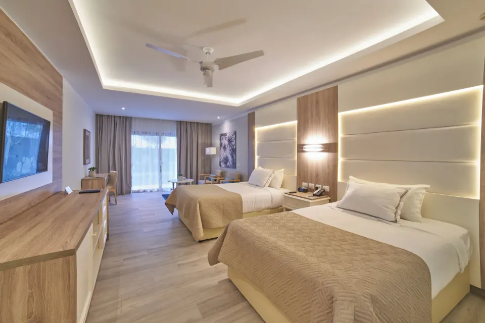 Junior Suite Deluxe with two beds, TV console, and balcony doors at Bahia Principe Escape Ambar.