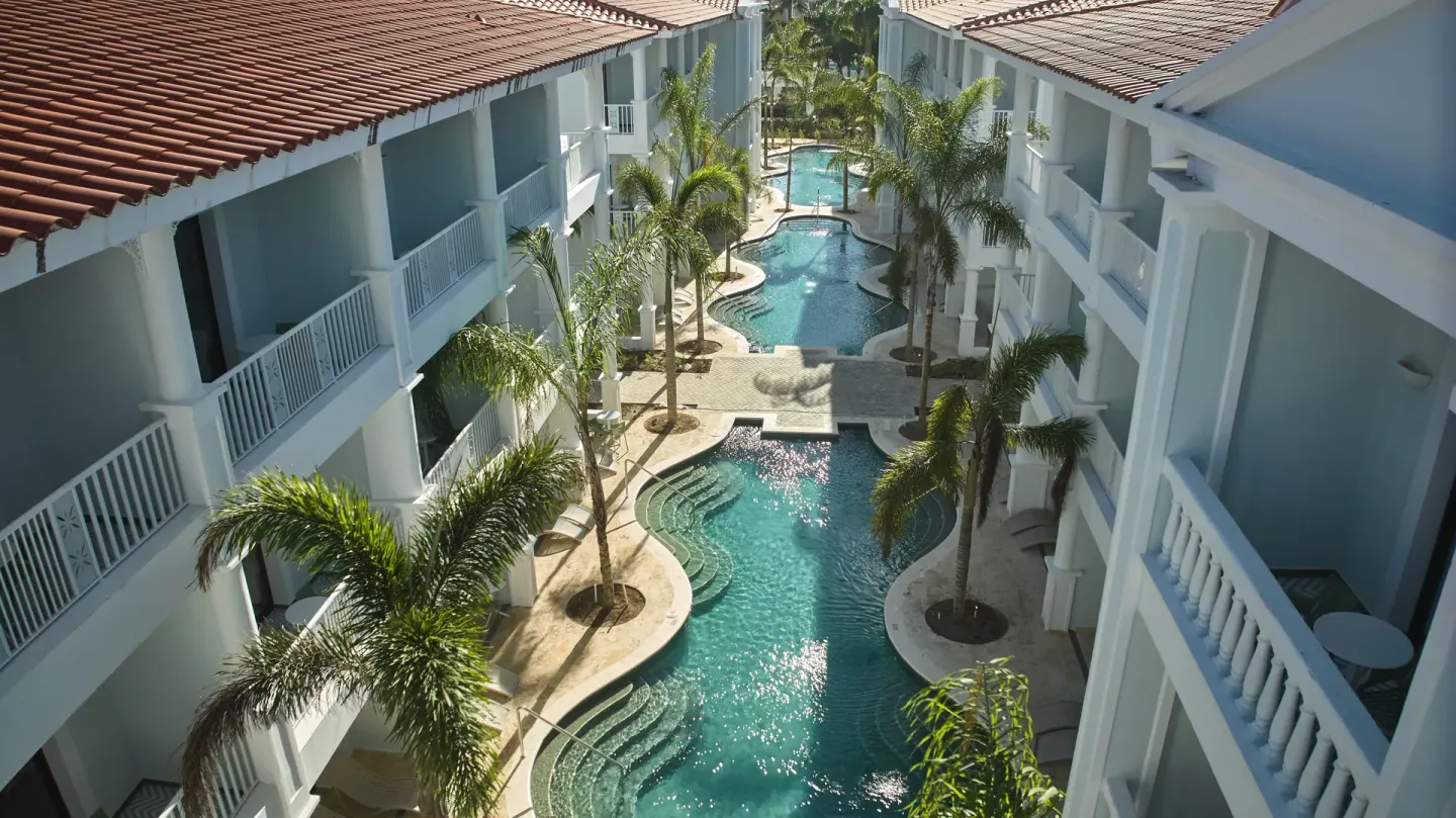 Aerial view of a winding swim-up pool between guest buildings at Bahia Principe Explore Esmeralda.