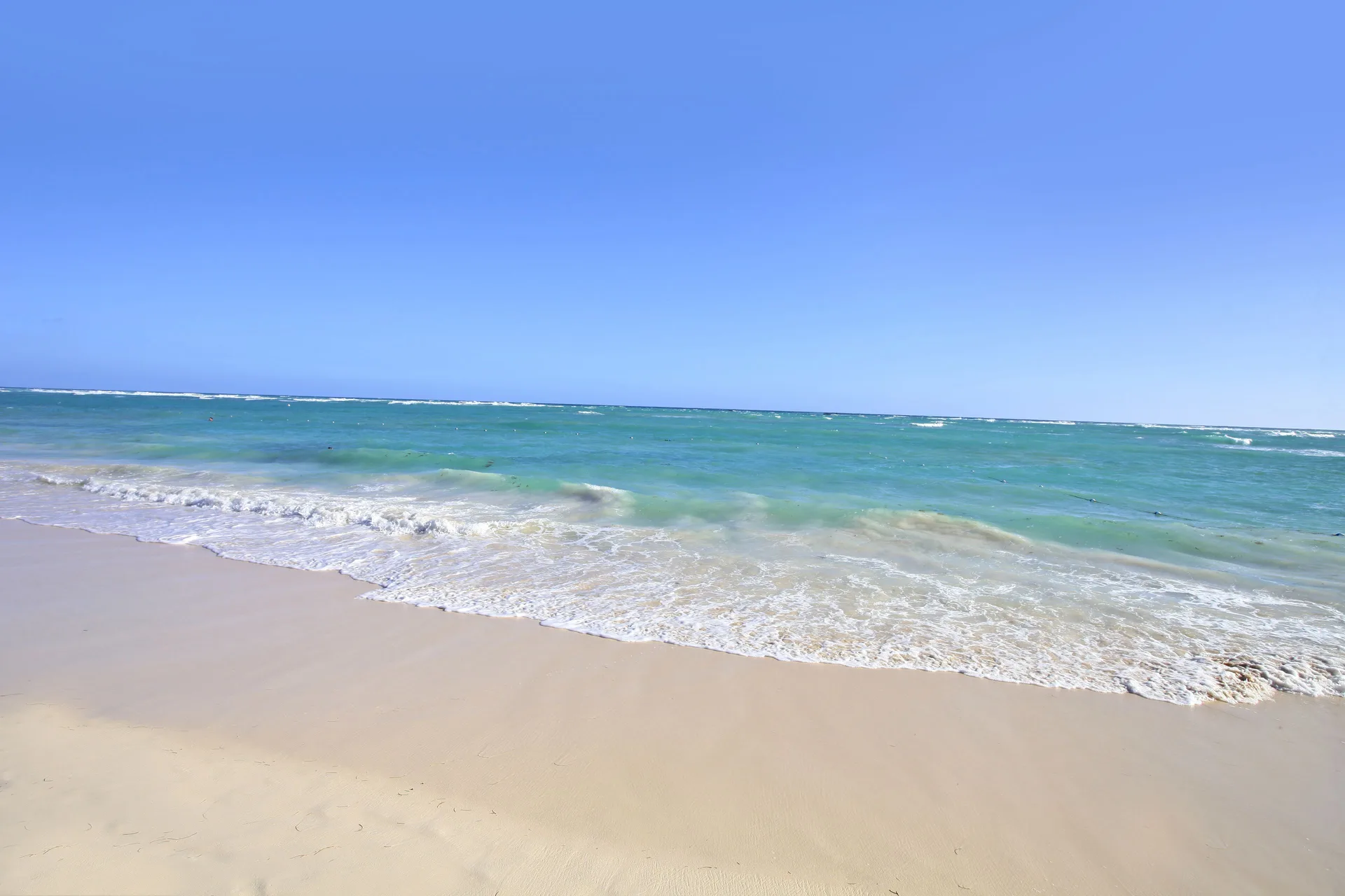 Sandy beach and turquoise surf at Bahia Principe Explore Esmeralda under a clear blue sky.