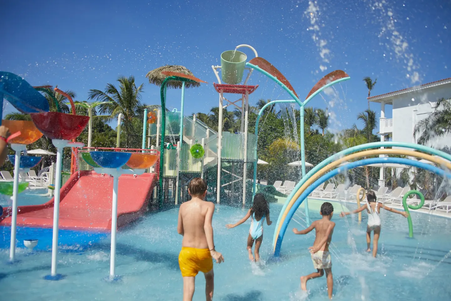 Children playing in a splash pool with slides and spray arches at Bahia Principe Explore Esmeralda.