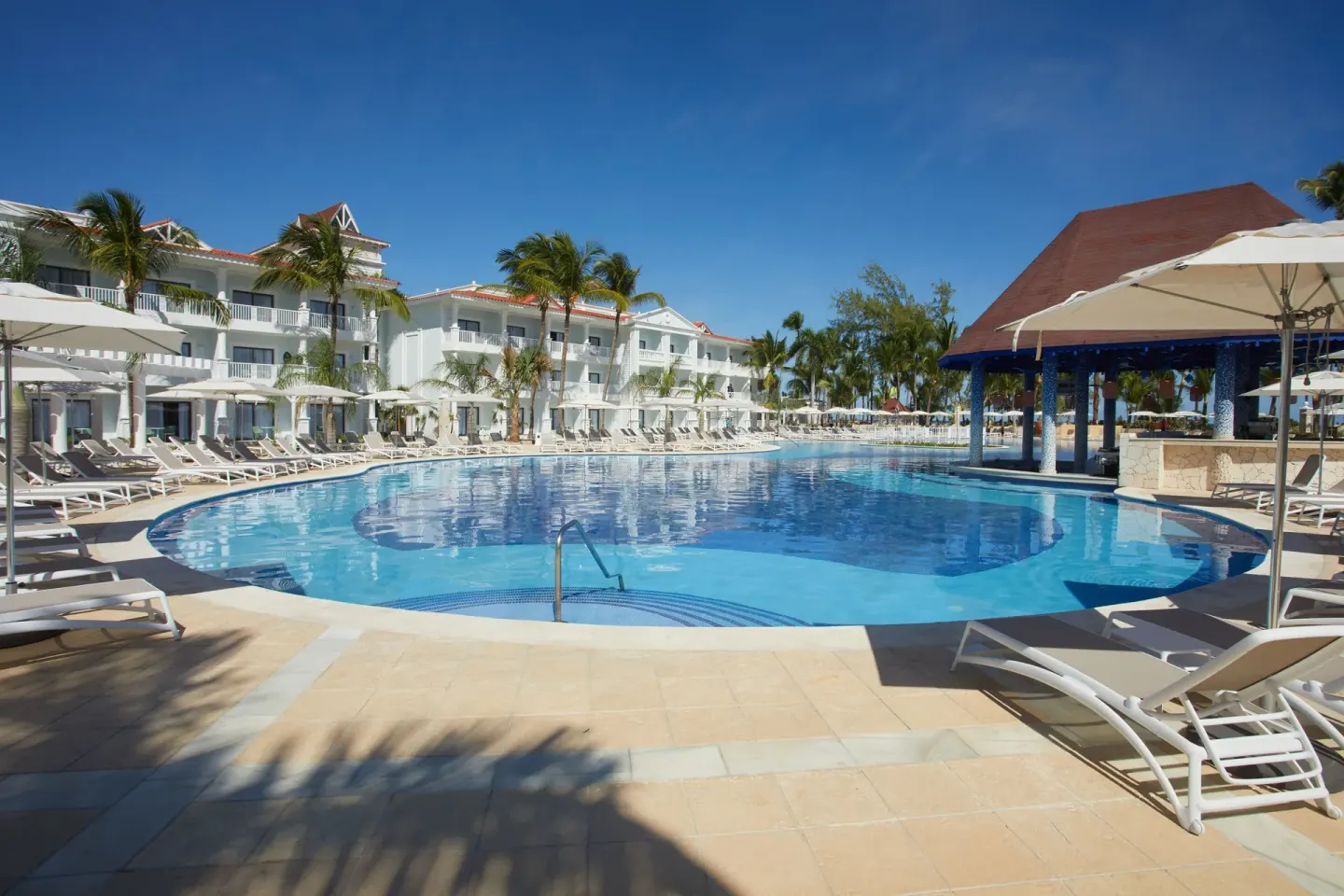 Curved pool, loungers and a red-roofed pavilion at Bahia Principe Explore Esmeralda.