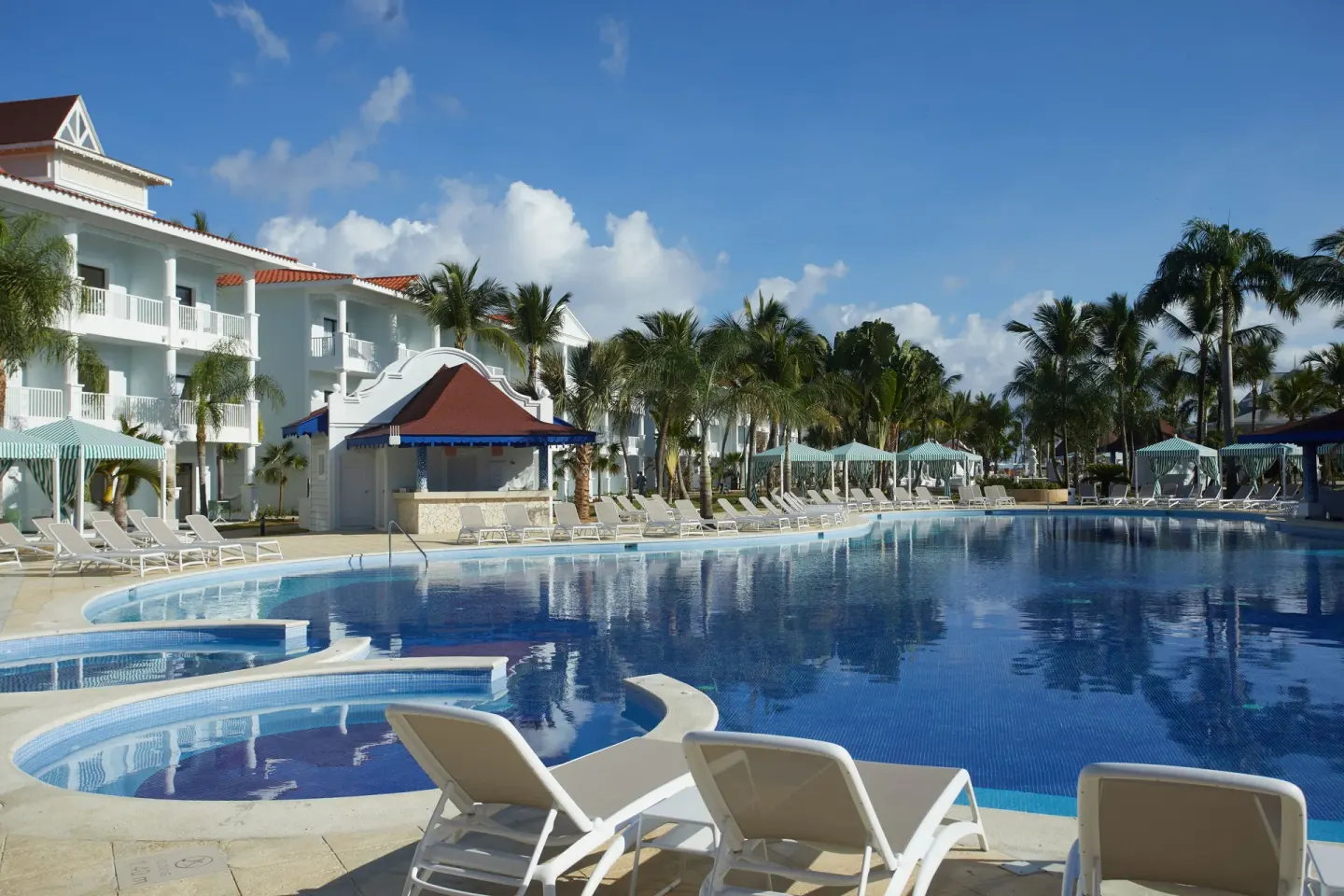 Curving resort pool with loungers and white buildings at Bahia Principe Explore Esmeralda.
