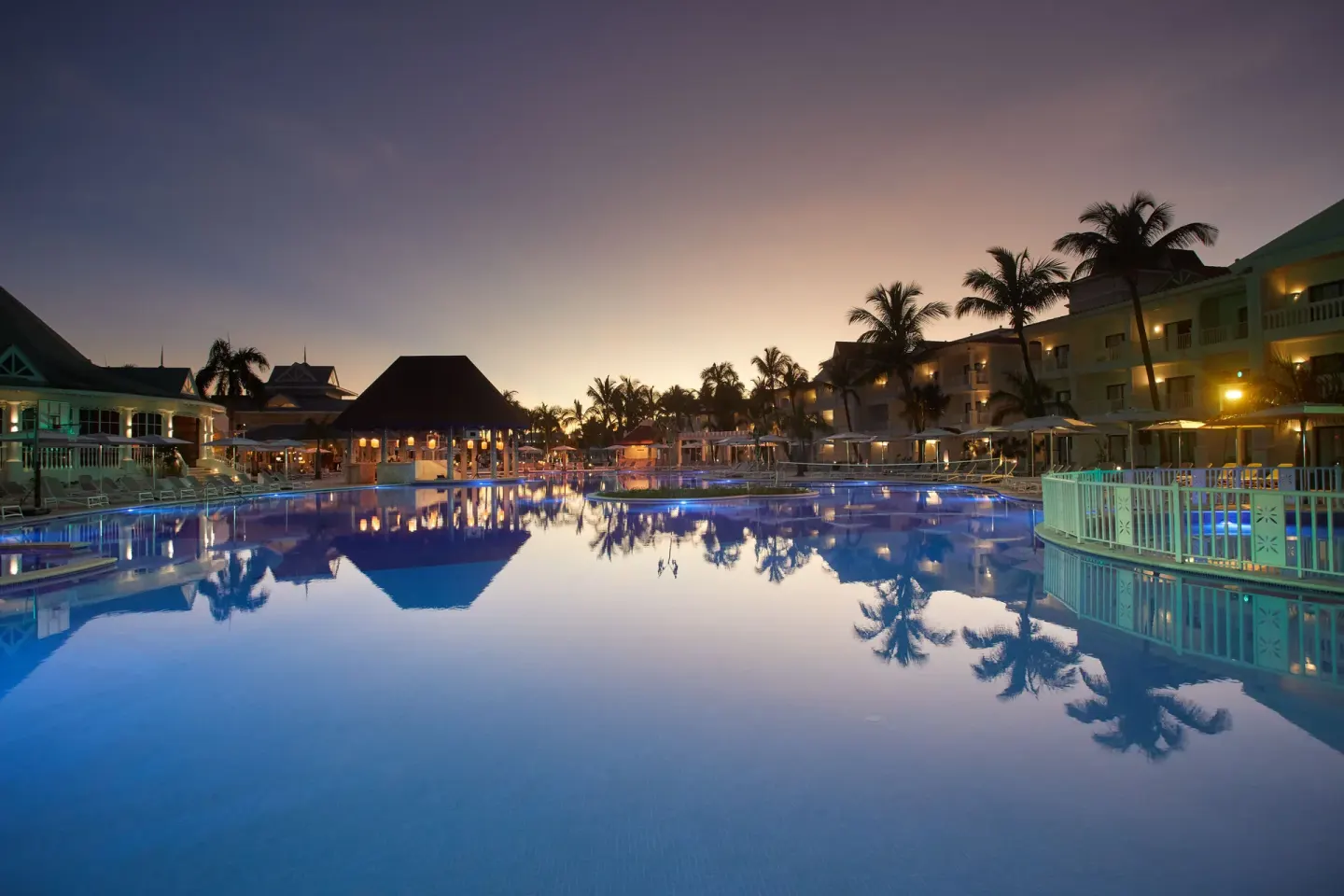 Wide dusk view of the pool and palm-lined buildings at Bahia Principe Explore Esmeralda.