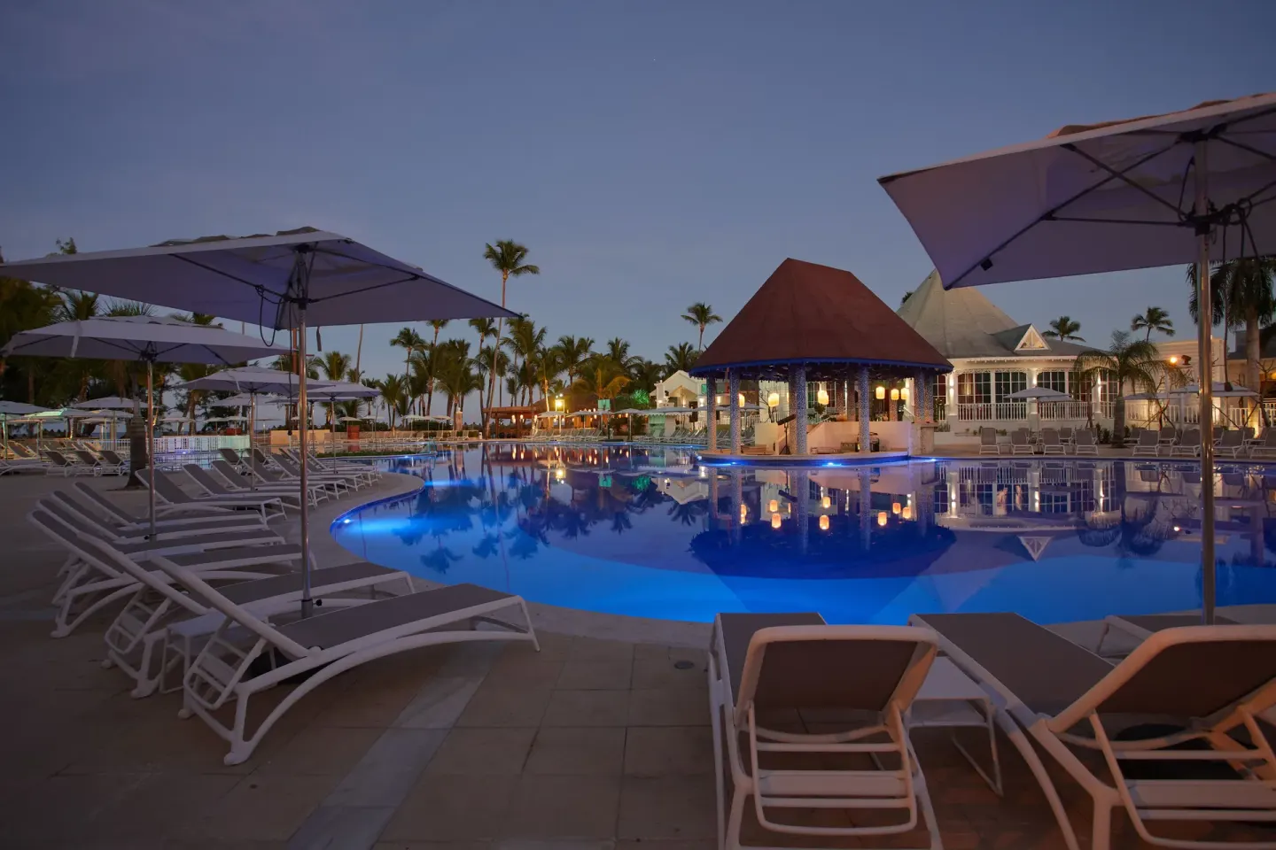 Evening pool with blue lighting, umbrellas and pavilion at Bahia Principe Explore Esmeralda.