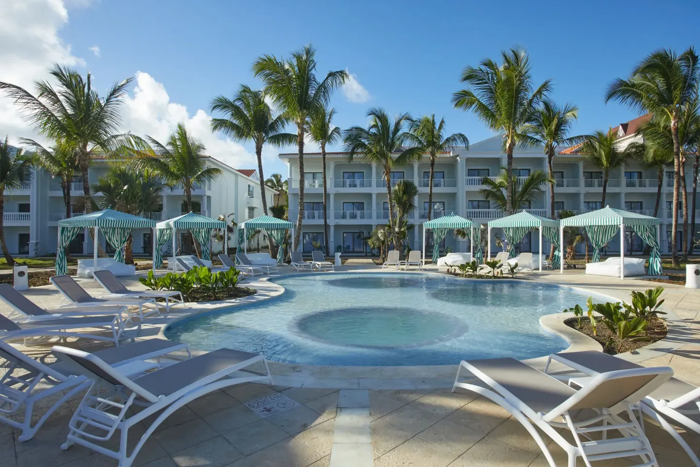 Resort pool with cabanas, loungers and palm trees at Bahia Principe Explore Esmeralda.
