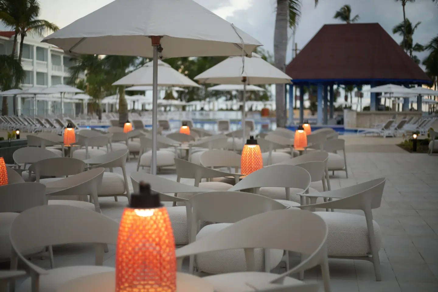 Poolside seating with umbrellas and glowing table lamps at Bahia Principe Explore Esmeralda.